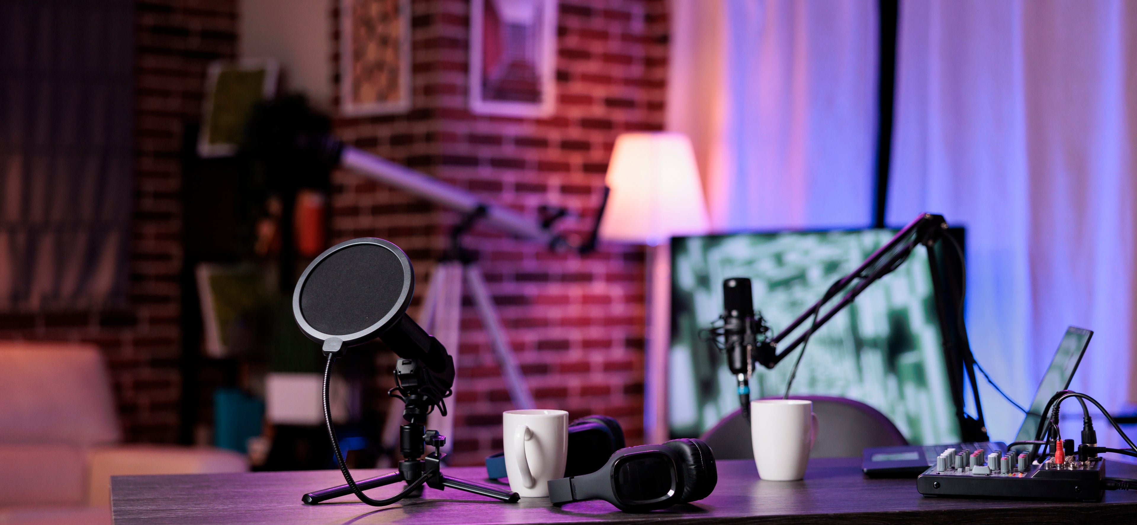 Home studio setup with microphone, headphones, and computer monitor in a room with brick wall and curtains.