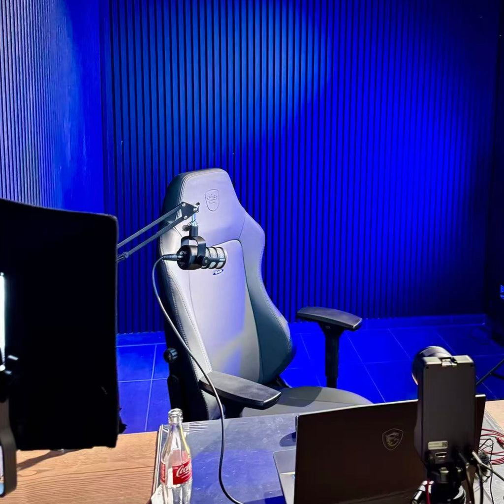 Gaming setup with chair, monitor, microphone, and Coca-Cola bottle against a blue wall.